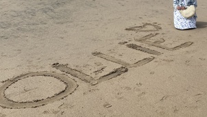 Image of a lady on the beach with the word Ollie written in the sand